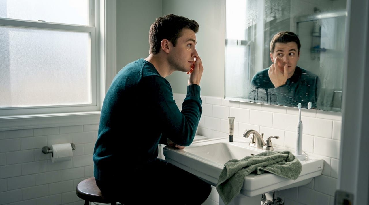 Man applying concealer in bathroom mirror