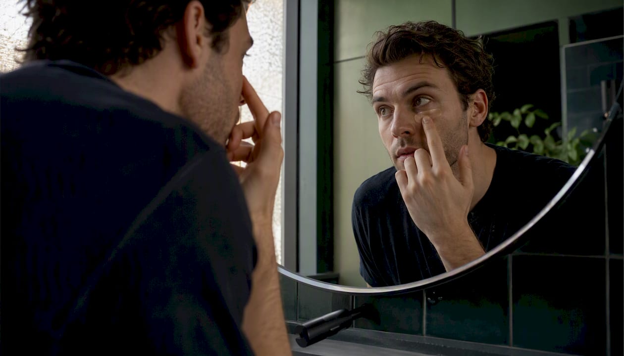 Man applying concealer in bathroom mirror